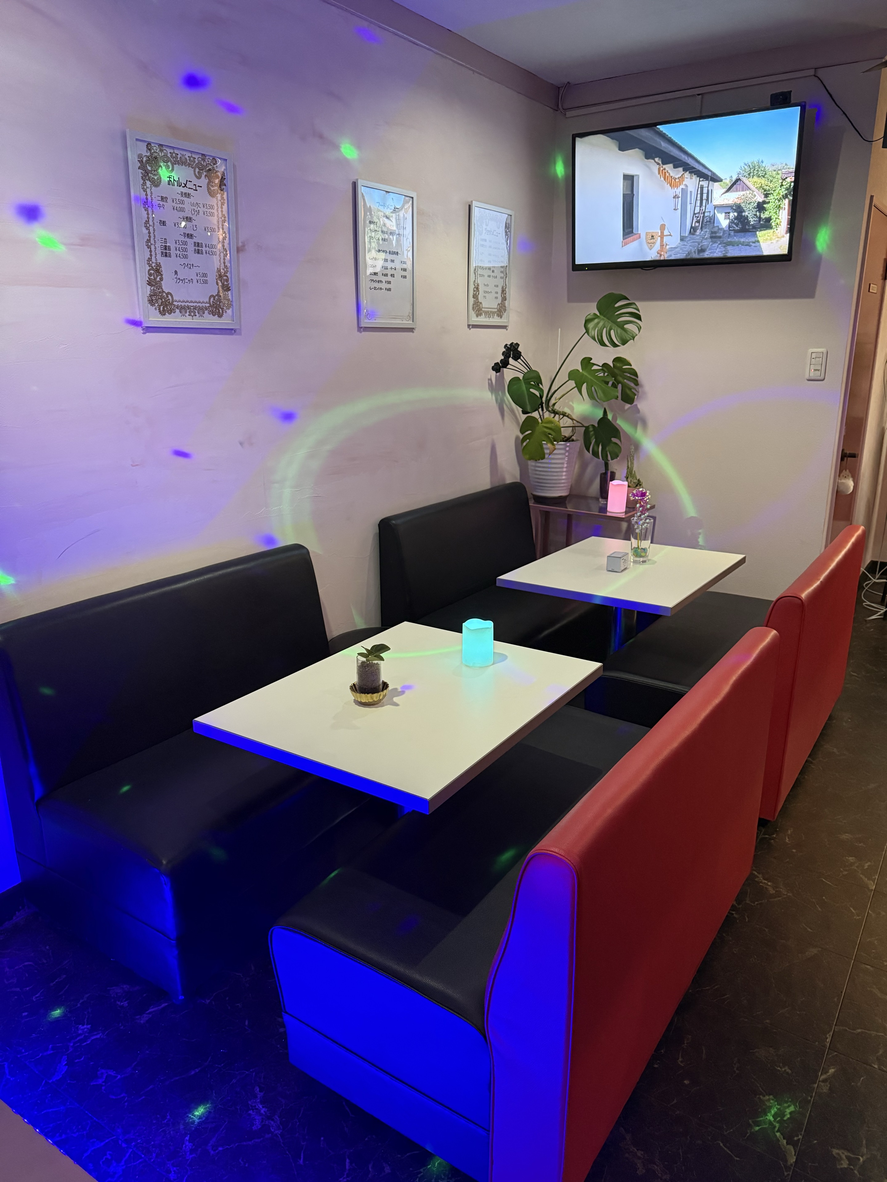 夜の店内に並ぶ、黒と赤のソファ席と白いテーブル。